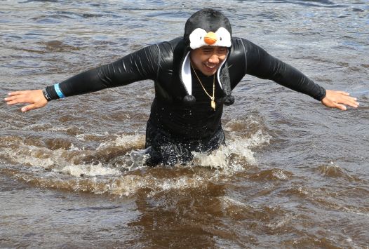 Young adult athlete wearing a black swim suit and a penguin hat running in the water.