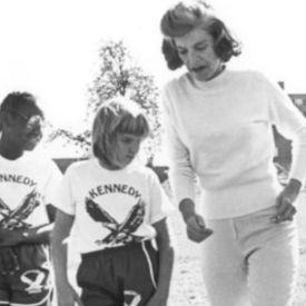 Black and white image of Eunice Kennedy Shriver teaching a young female and male athlete