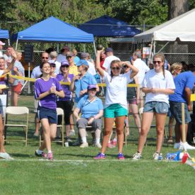 Individuals standing on the grass outside cheering.