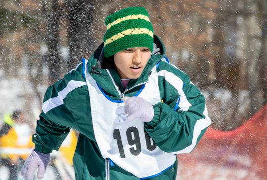 Young athlete wearing a winter hat and coat running in the snow.