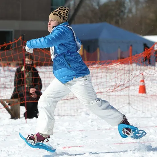 Athlete wearing white pants and a blue winter jacket skiing in the snow.