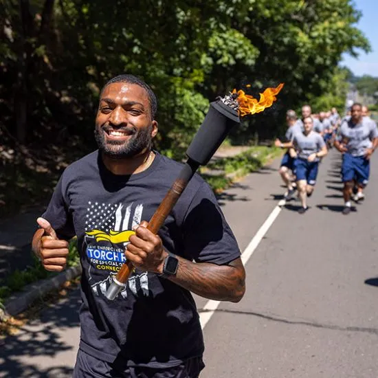 Man running on the road wearing a black t-shirt and smiling while holding a torch.
