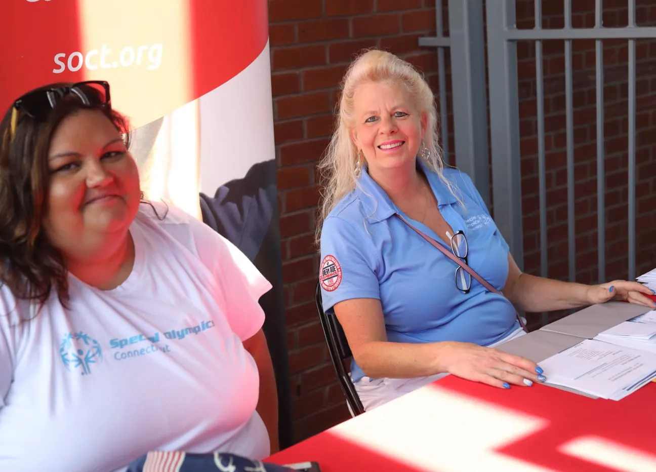 Two women sitting at a table outdoors, wearing Special Olympics shirts.