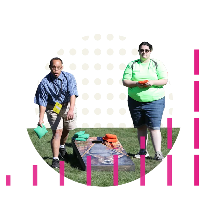 Male and female athletes playing corn hole on a grass lawn.