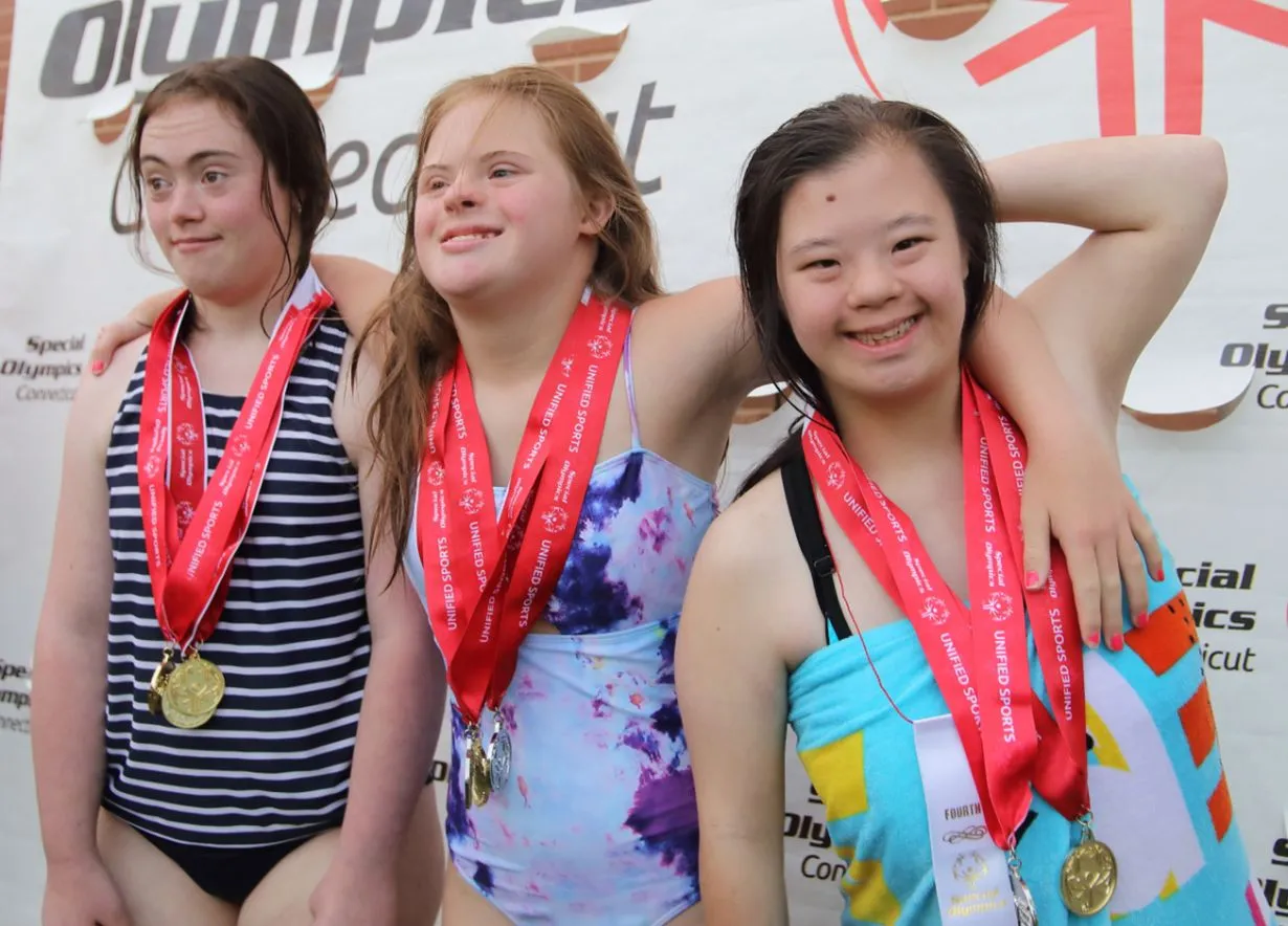 Female athletes smiling together wearing bathing suits and medals around their necks.