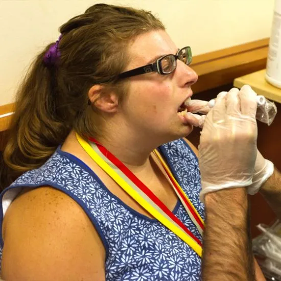 Female athlete wearing blue and white tank top and glasses having her throat checked at the doctor.