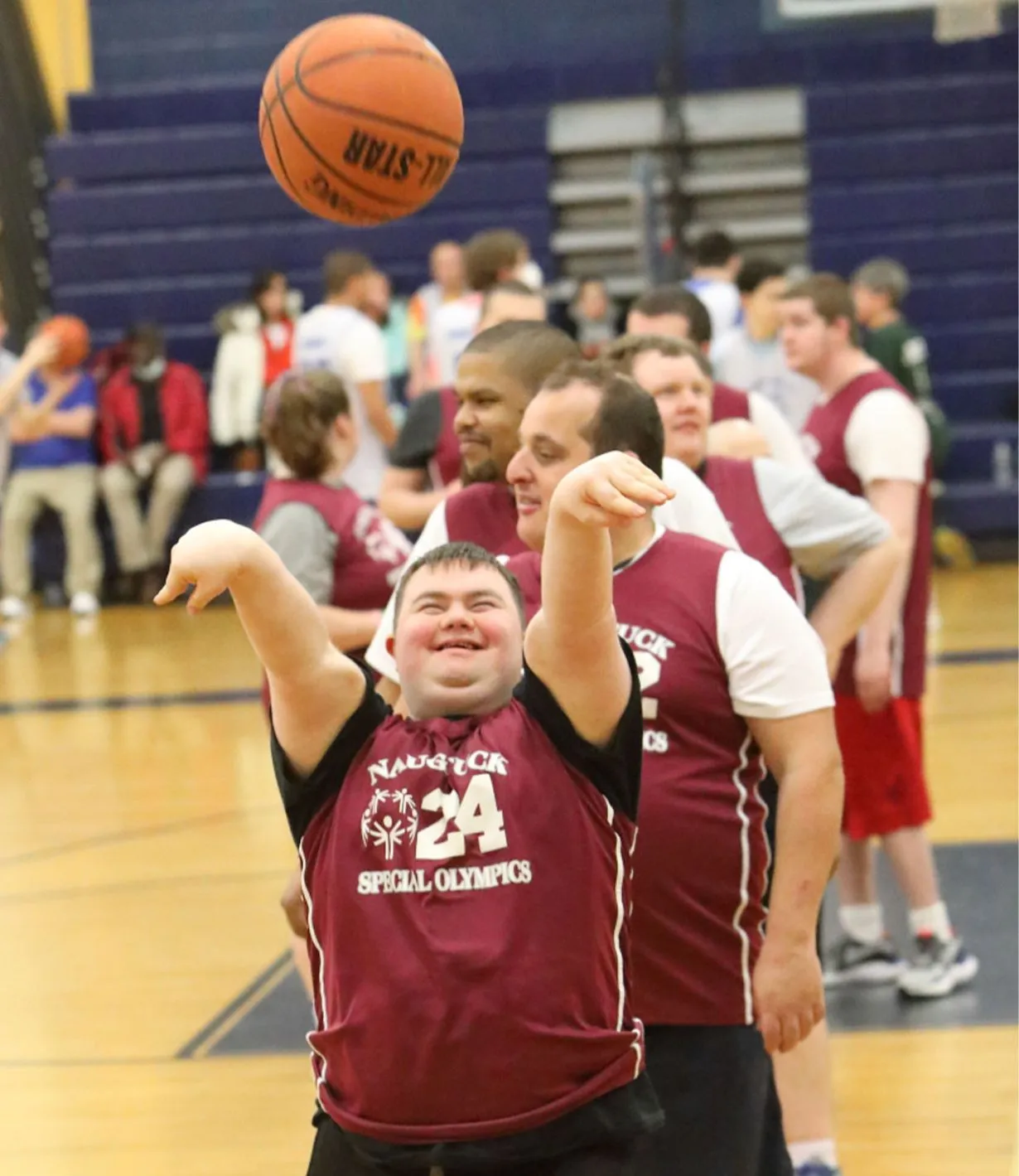 Male athlete shooting a basketball wearing a Naugatuck Special Olympics maroon jersey.
