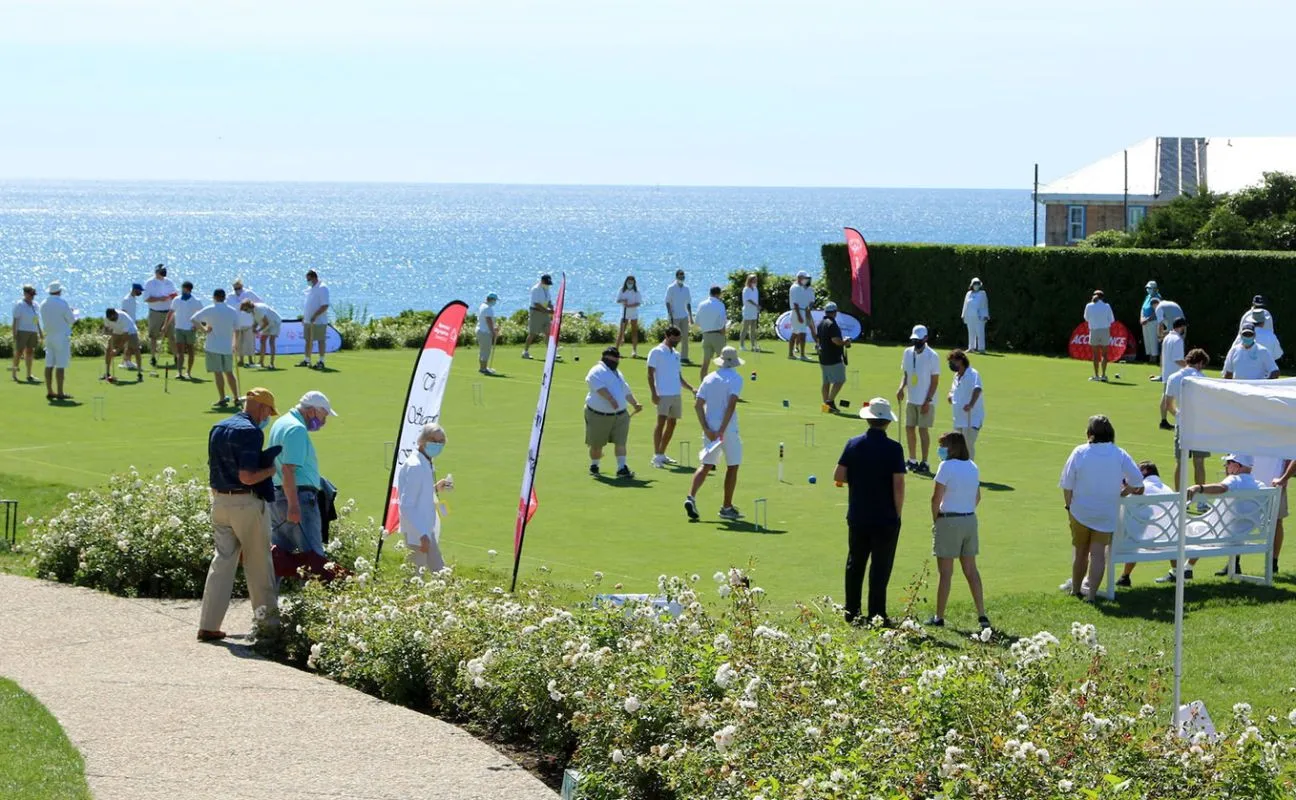 Group of individuals wearing white shirts playing golf at a course surrounding a body of water.