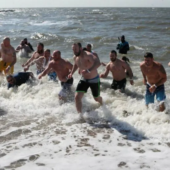 Men running out of the ocean on a sunny day with swim trunks on.