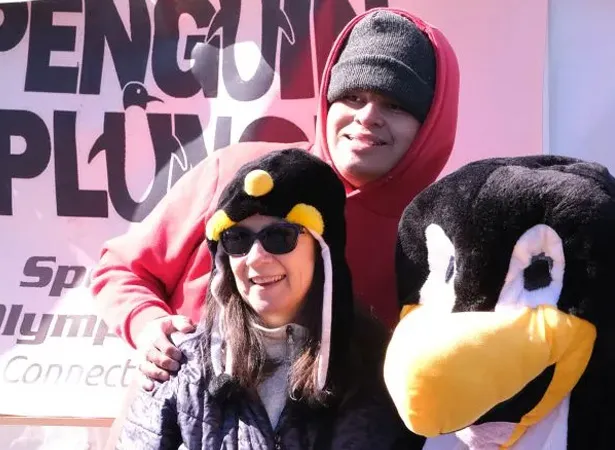 Two adults posing with penguin mascot in front of Penguin Plunge banner.