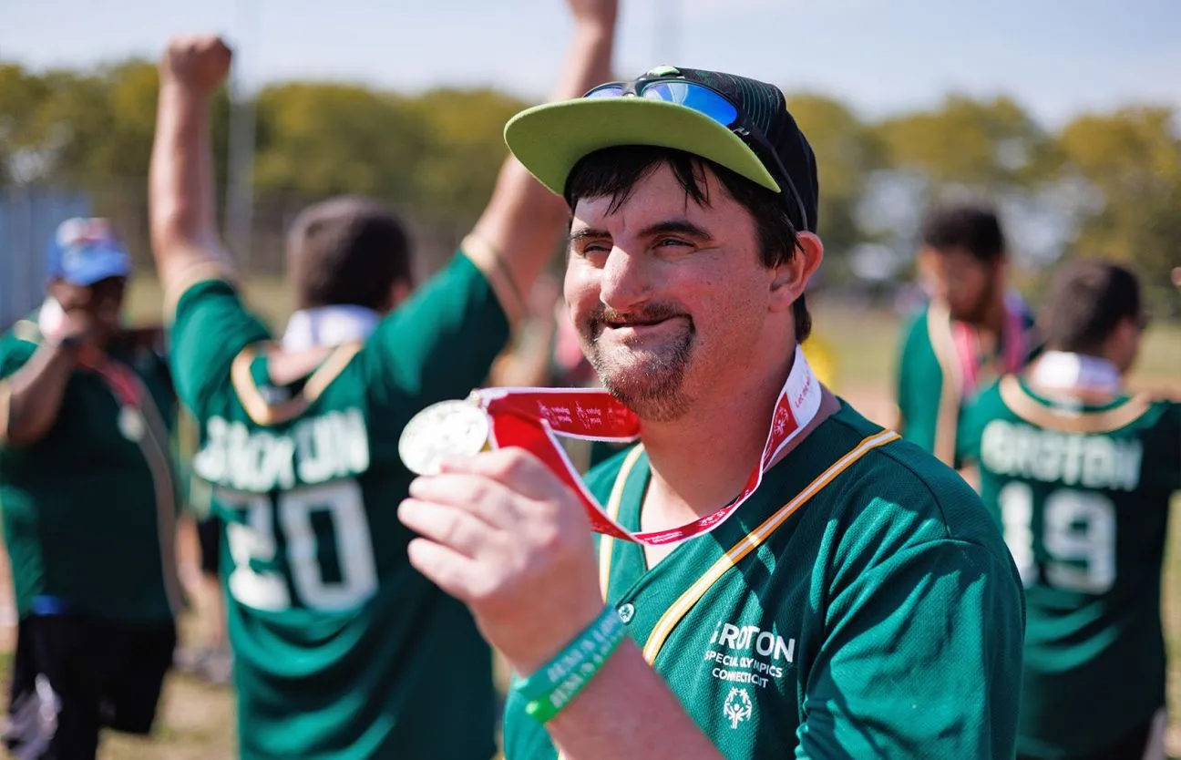 Male smiling by a body of water wearing a teal bowtie and red tropical shirt.