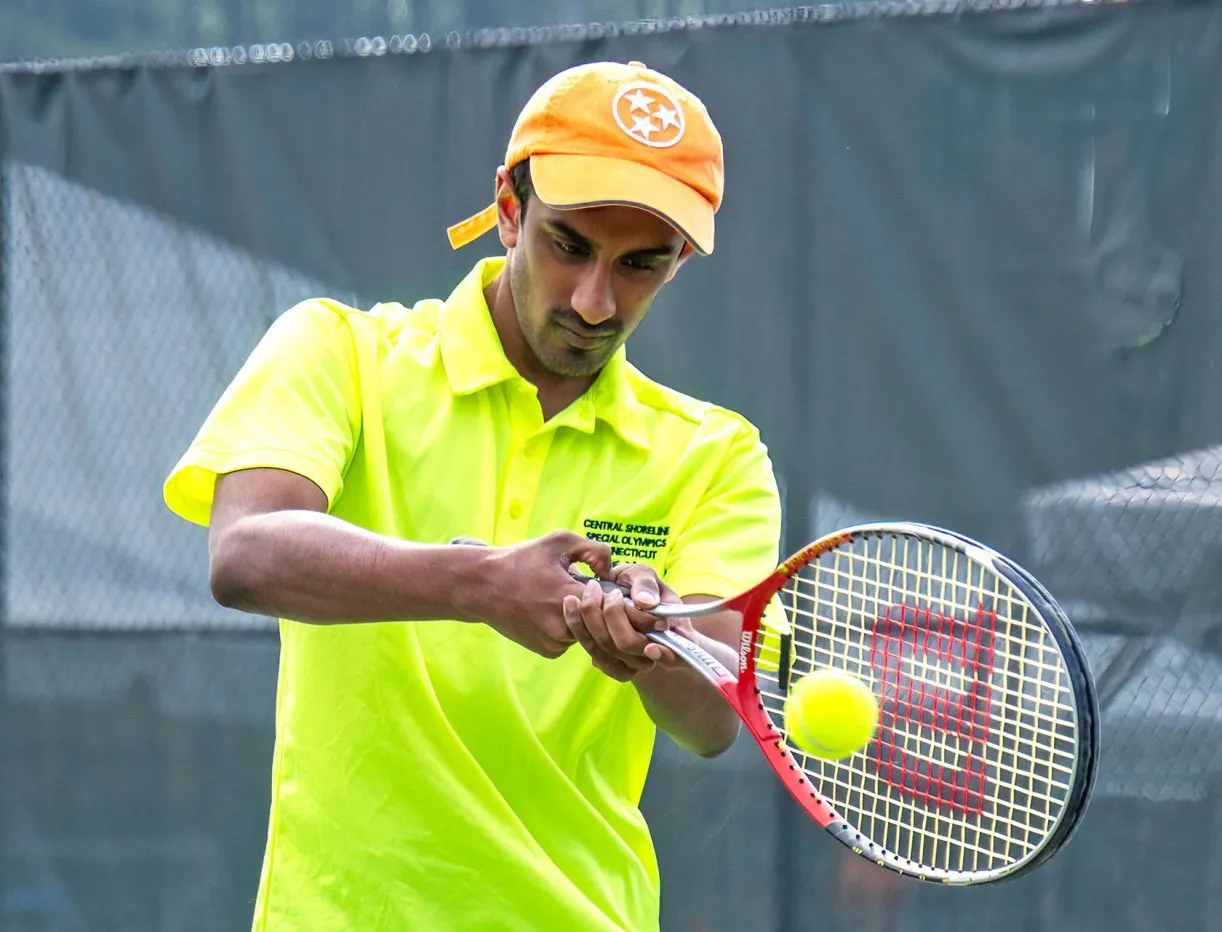 Male athlete in a neon yellow shirt swinging at a tennis ball with a tennis racket 