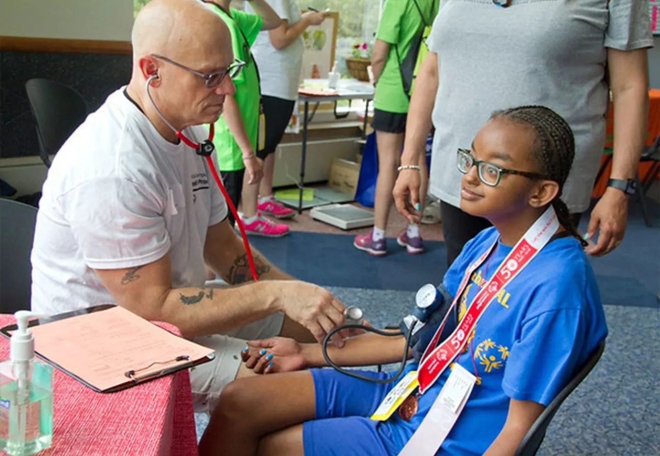Male and female standing behind a table with a blue table cloth that has healthy food options displayed.