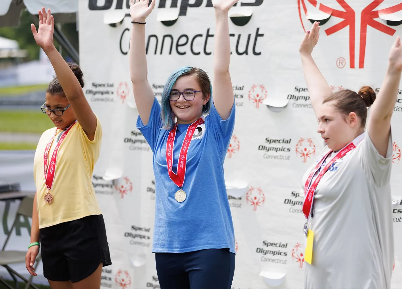 Three athletes standing on podium with hands raised