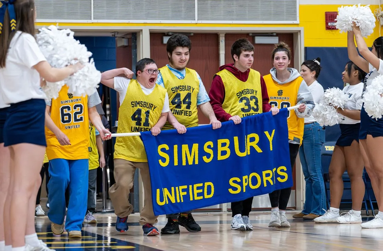 Two male and three female athletes posing with medals around their necks on a grass field.