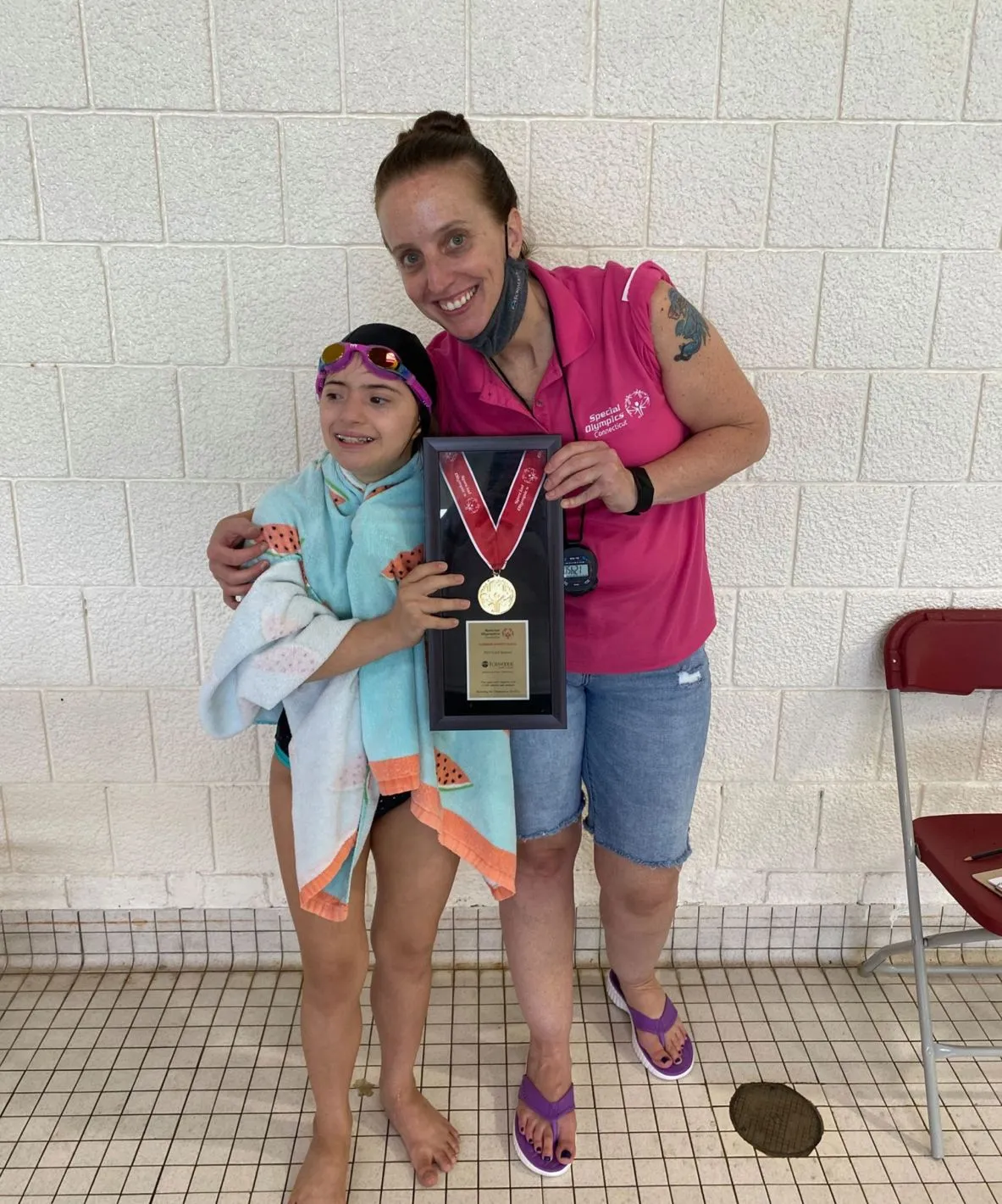 Female coach and youth swim athlete smiling holding a framed metal together.