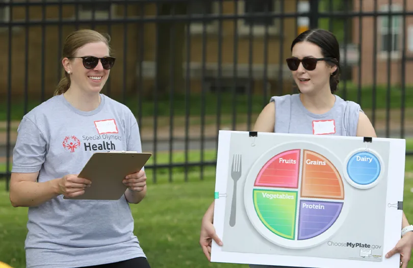 Special Olympics Health Directors standing outside wearing grey t-shirts and sunglasses holding a diagram