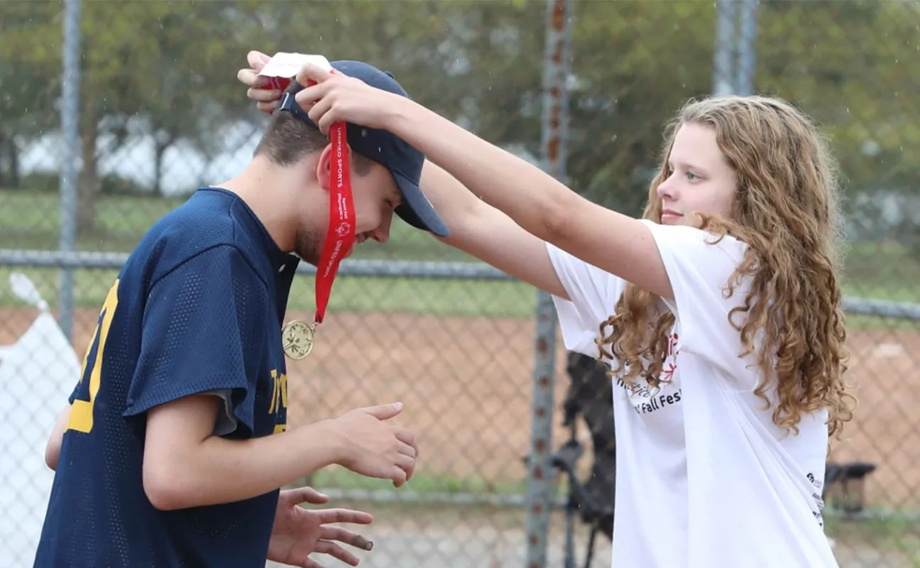 Young volunteer presenting an athlete with a medal by placing it over his head.