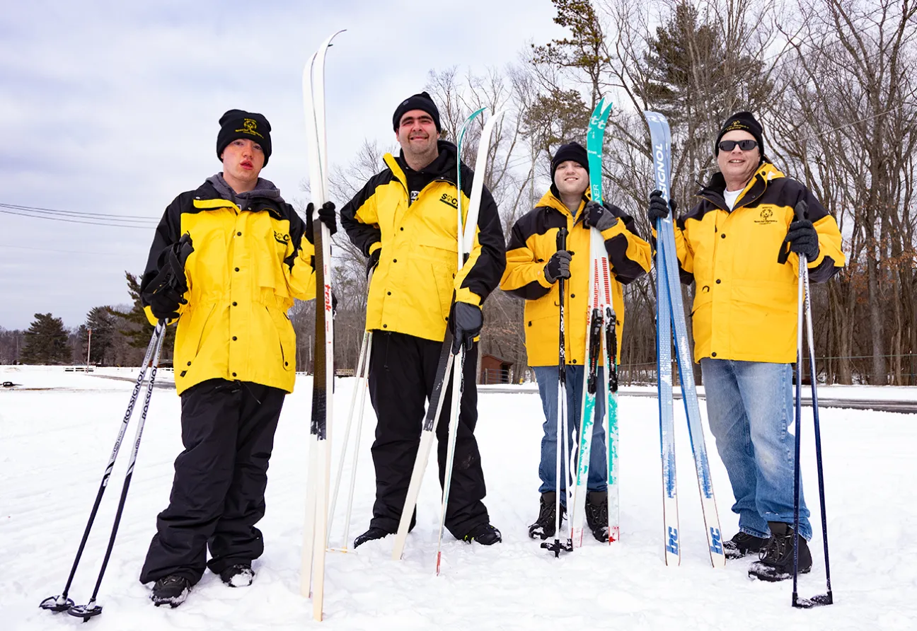 Athletes standing in the snow holding skis and wearing yellow winter jackets.